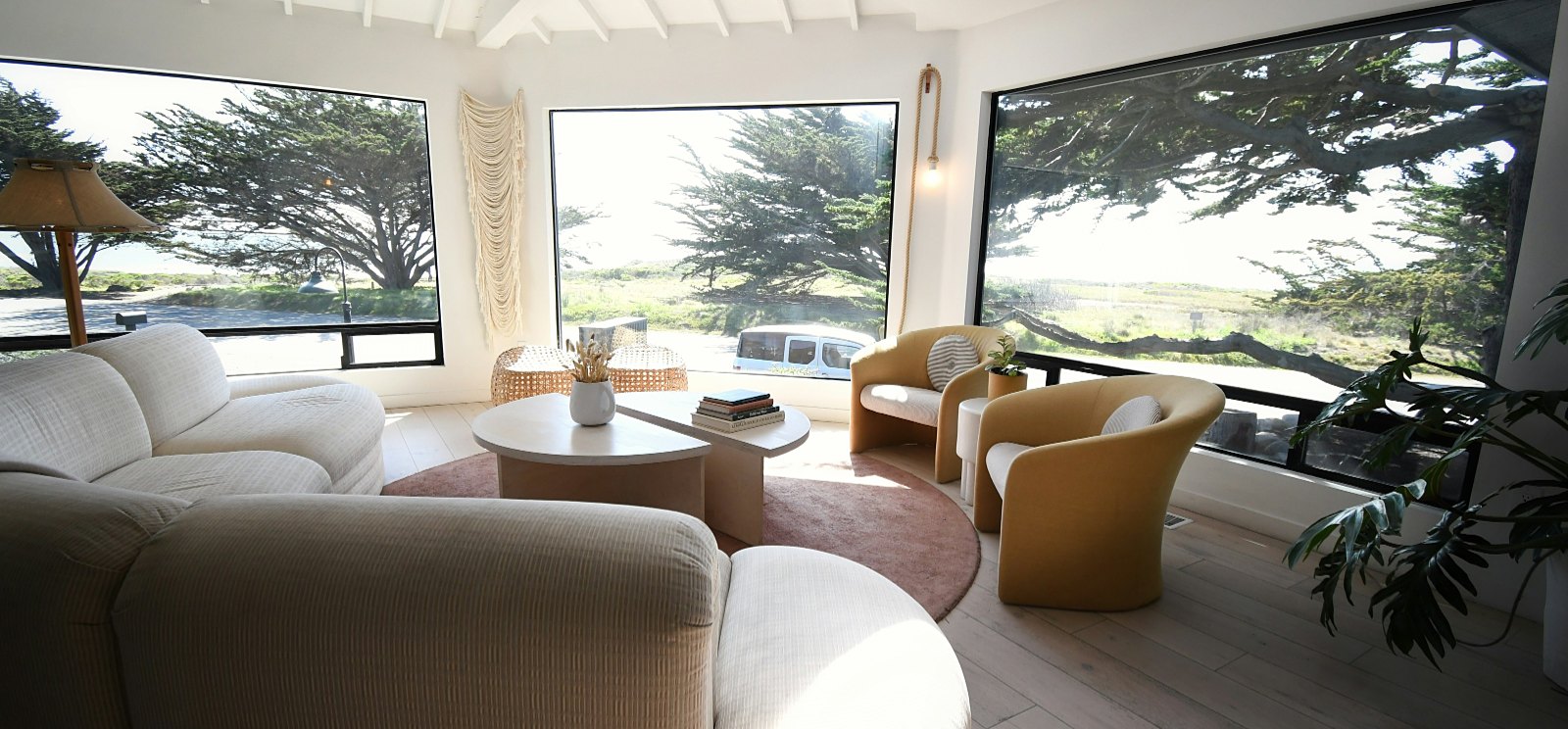 A living room with wide windows onto cypress trees and open land