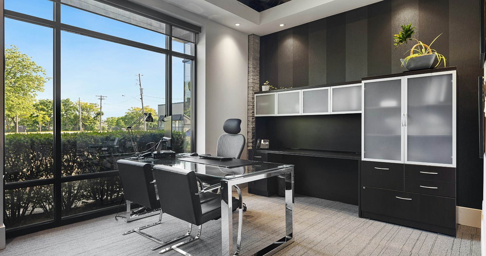 A modern private office with a desk, guest chairs and a window onto greenery